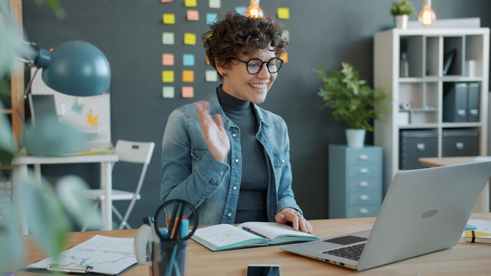 Product designer waving during a live video call in a creative studio